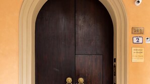 Uma porta de madeira escura com duas maçanetas de latão, uma porta em arco e um chão de azulejos.