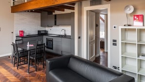 Uma sala de estar moderna com um sofá de couro preto, piso em padrão herringbone de madeira e vigas de madeira aparente no teto.