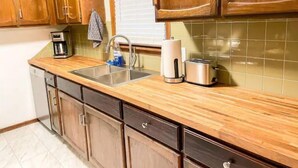 A kitchen with wooden cabinets, a stainless steel sink, a coffee maker, a toaster, and a window with blinds. - Lovely Home! Great Location! The Nature House (Springfield)