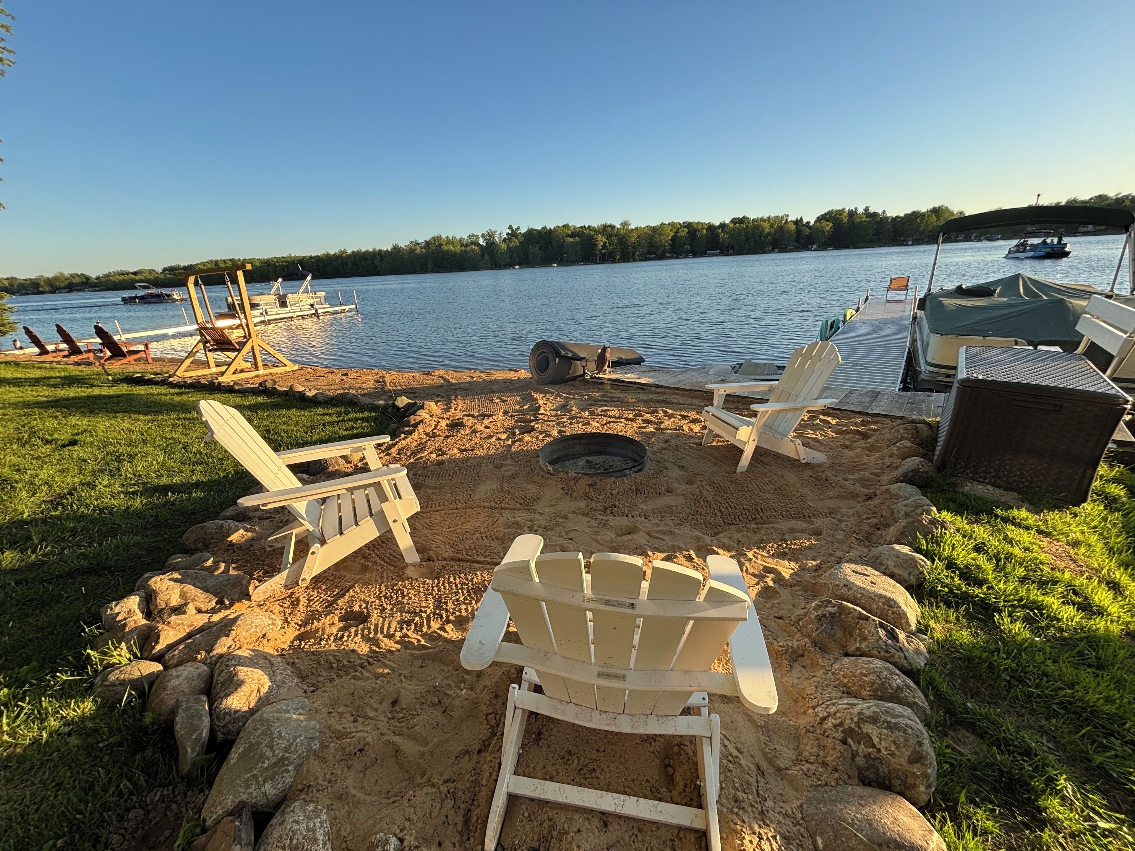 A lakeside deck with Adirondack chairs, a fire pit, and a boat dock.