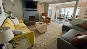 A living room with a sofa, armchair, and a television mounted on the wall.