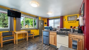 Eine kleine Küche mit Holzmöbeln, einer Mikrowelle, einem Kühlschrank und einem Essbereich mit einer Bank und einem Tisch.