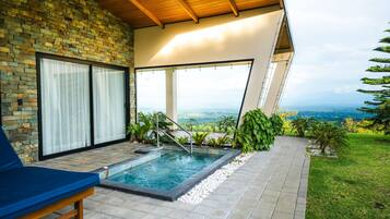 A modern outdoor pool area with a stone wall, a blue lounge chair, and a view of the landscape.