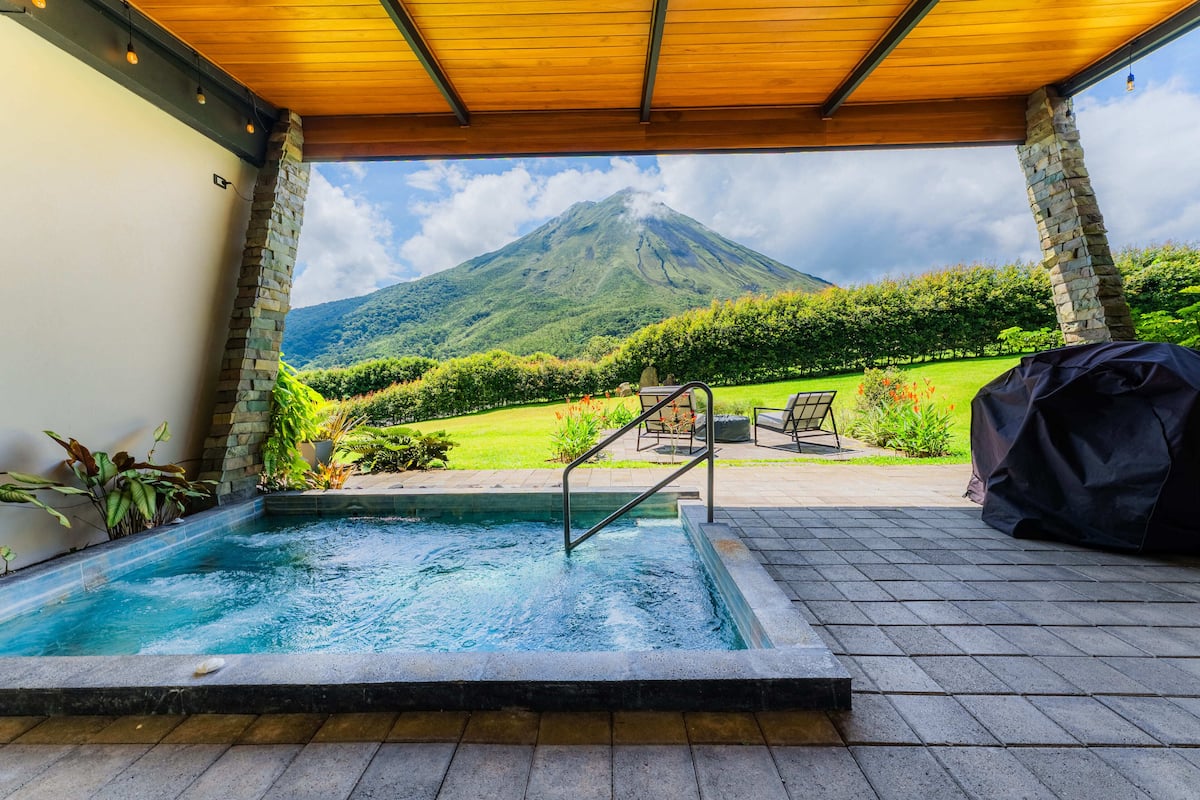 A pool area with a view of a mountain, stone pillars, and outdoor furniture.