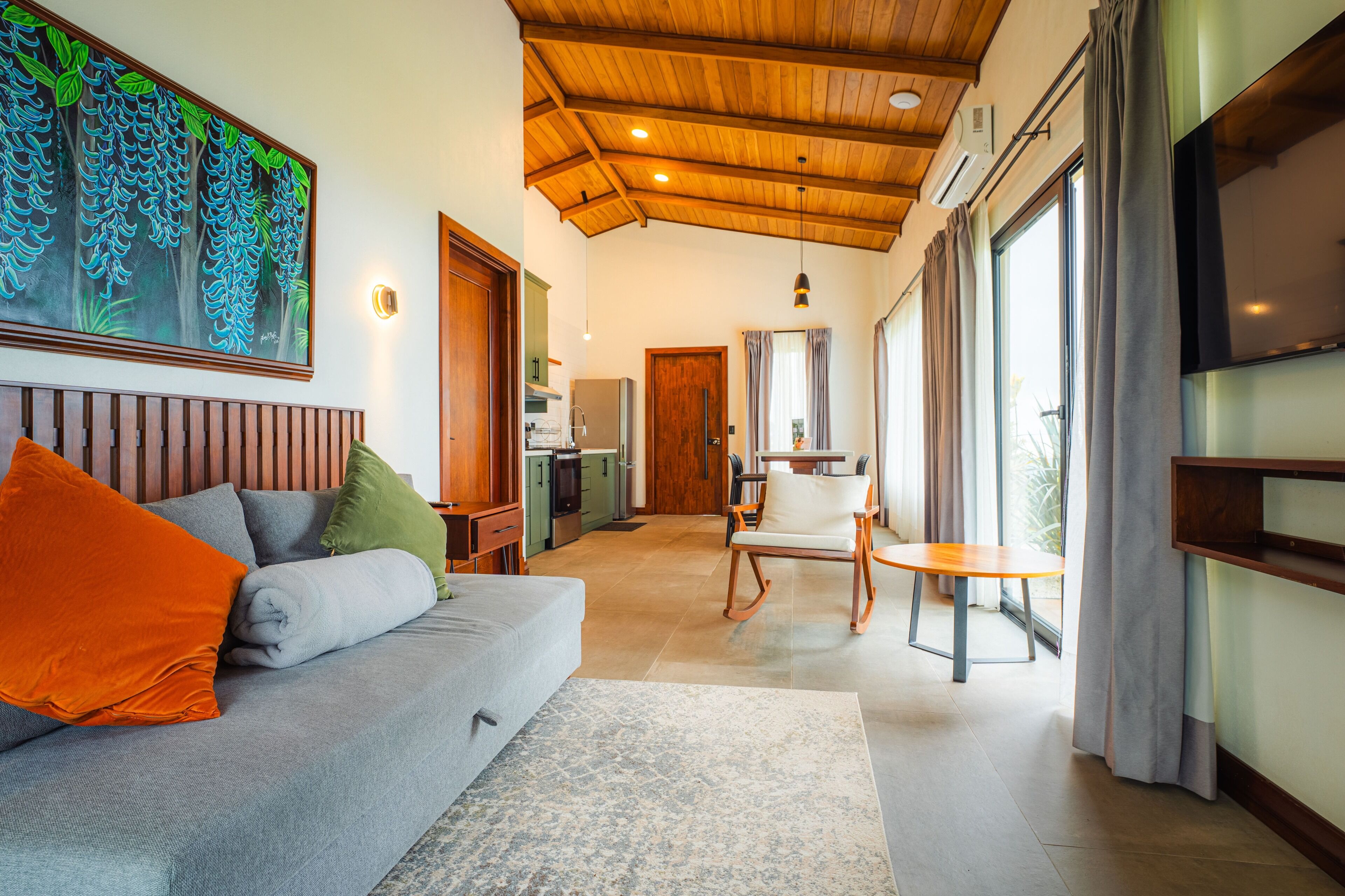 Ein modernes Wohnzimmer mit einem grauen Sofa, einer Holzbalkendecke und einem großen Fenster mit Vorhängen.