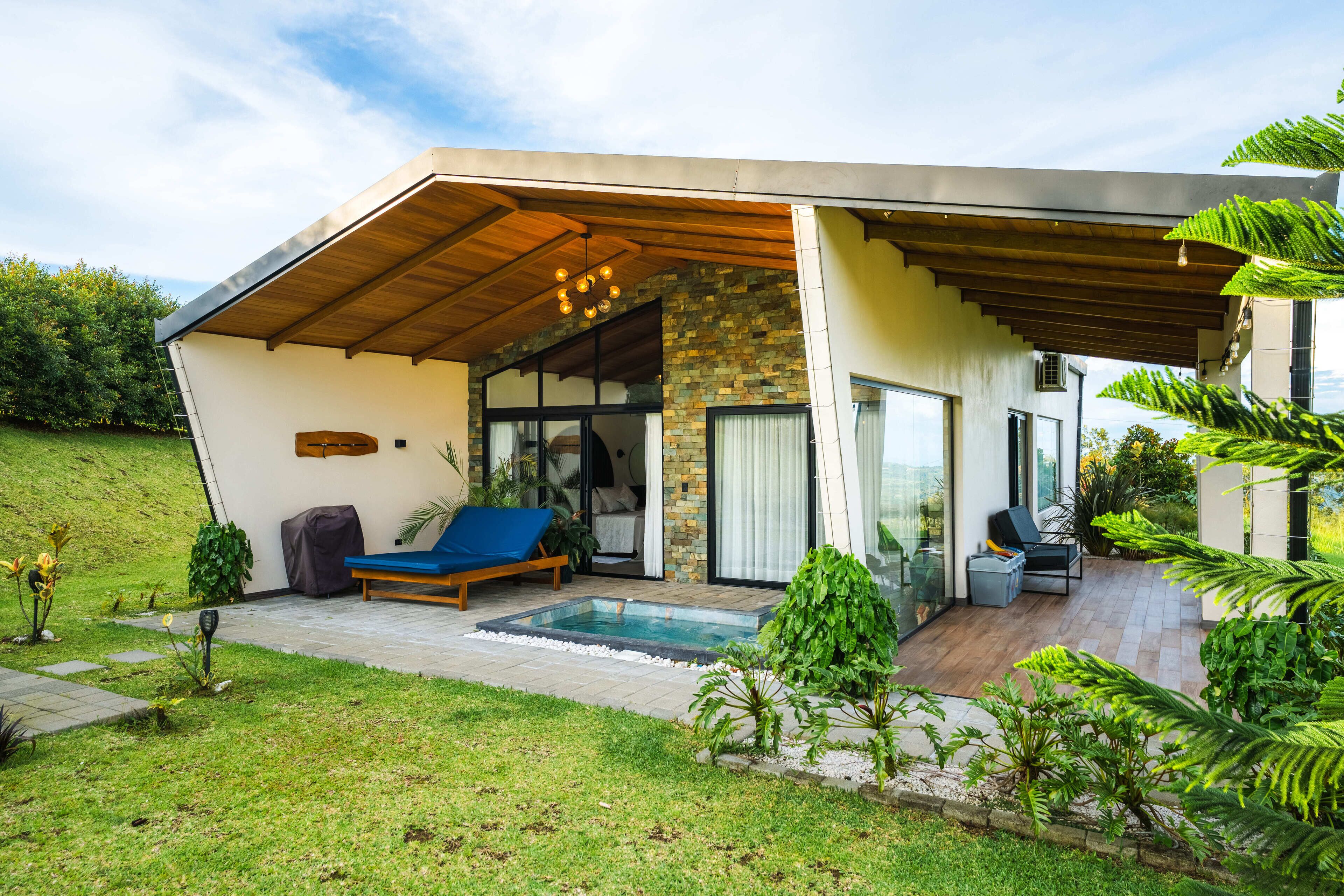 A modern house with a covered patio, a swimming pool, and a lush garden.