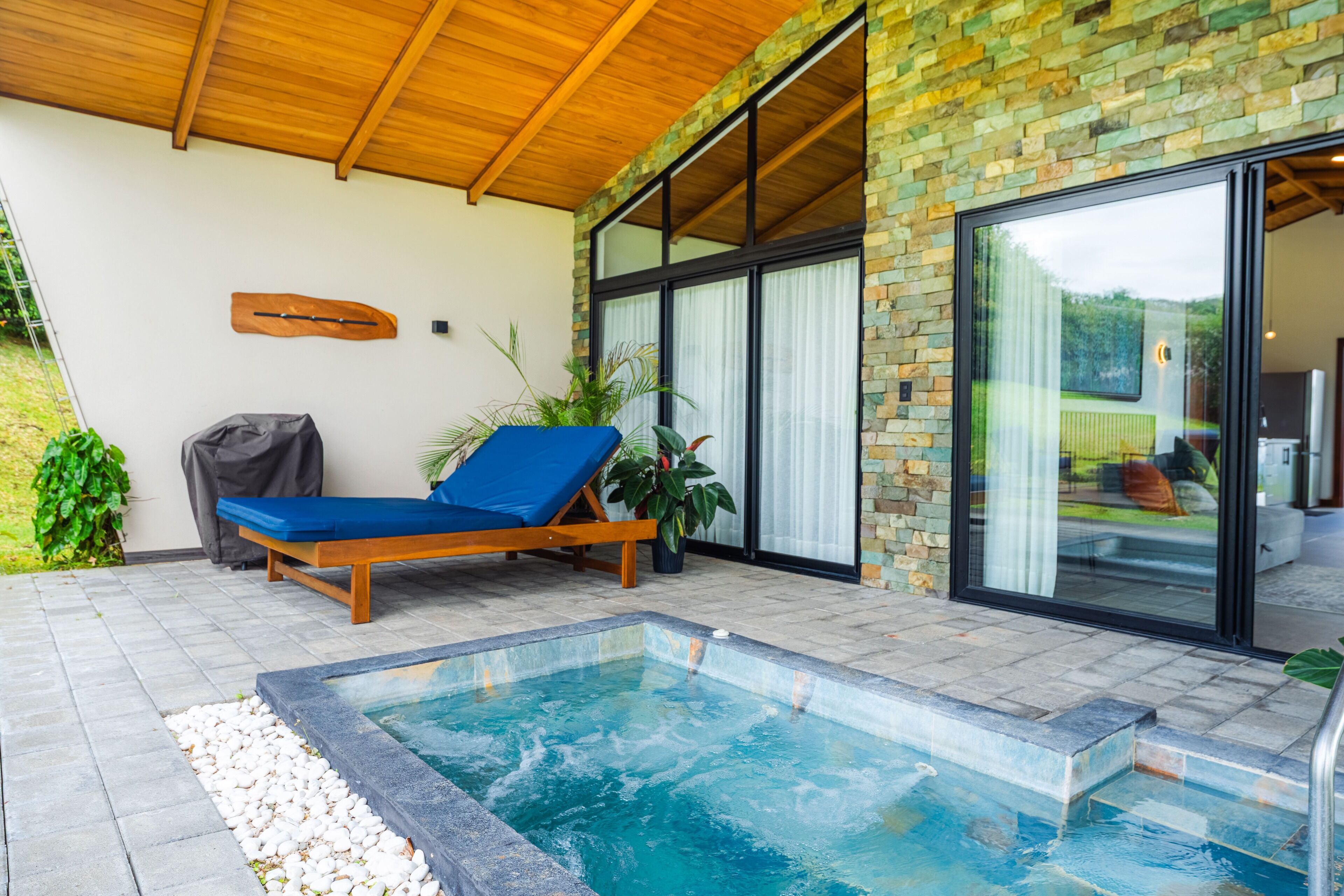 Un área de piscina moderna al aire libre con terraza de madera, una silla de descanso y una piscina pequeña.