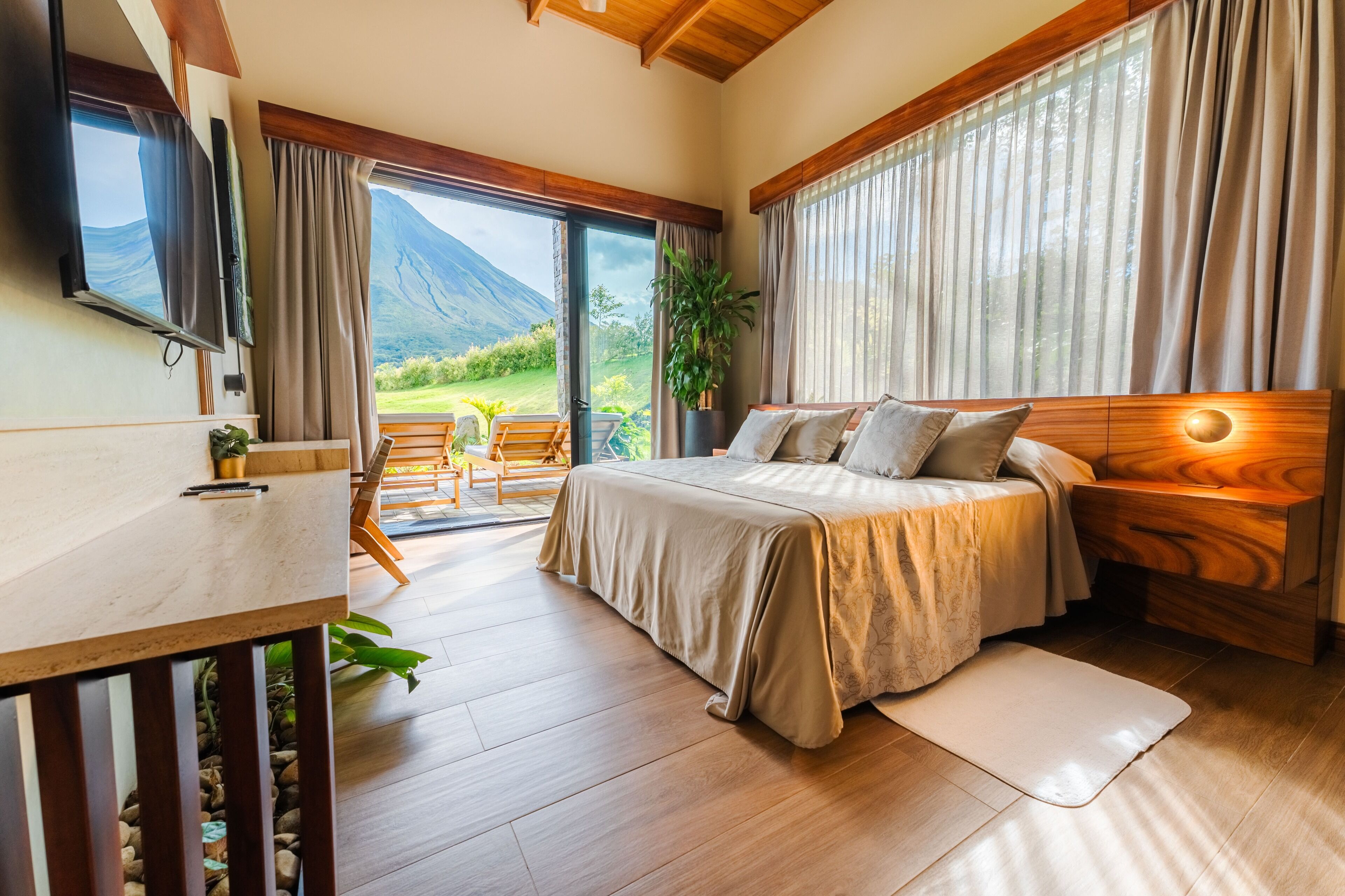 Een slaapkamer met een bed, een bureau, een televisie en uitzicht op een berg.