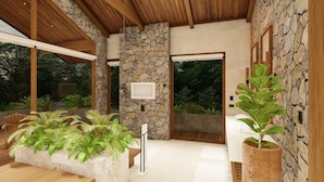 A modern interior with a stone wall, wooden ceiling, and large windows. - Villas Jawara (La Fortuna)