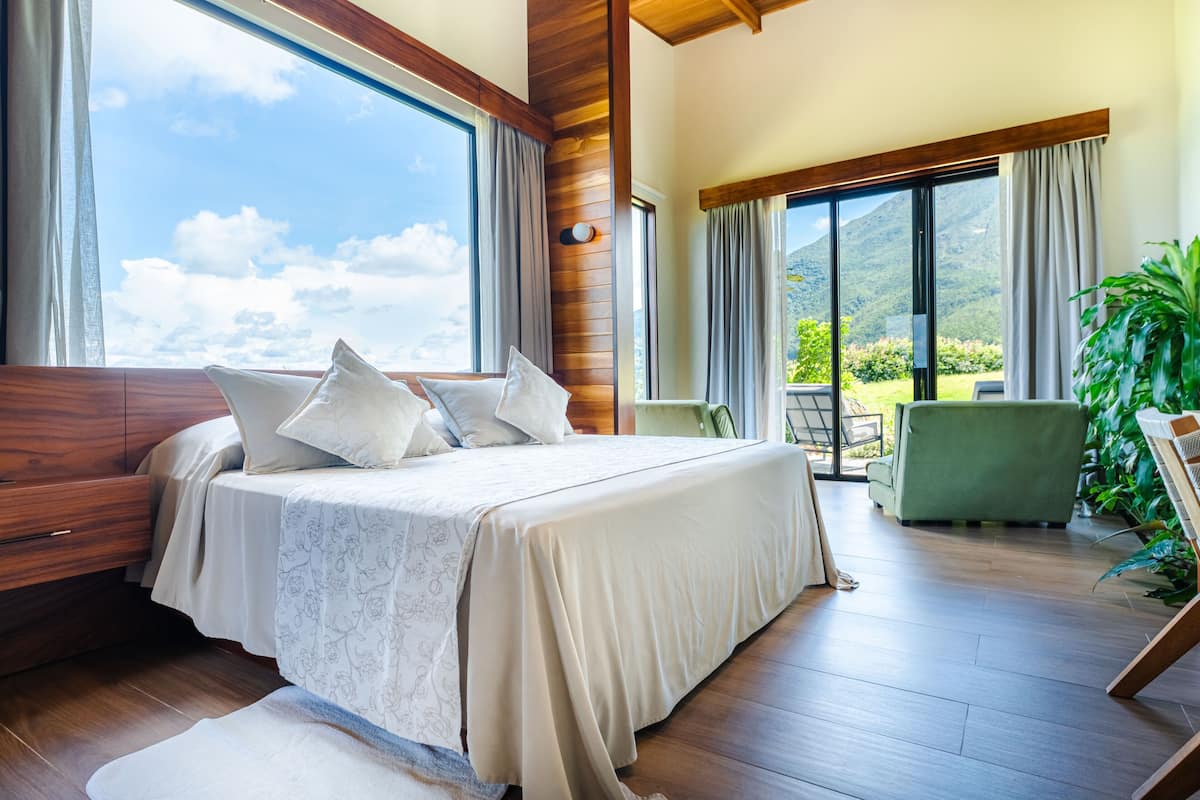 A bedroom with a large bed, wooden flooring, and a view of a mountainous landscape through large windows.