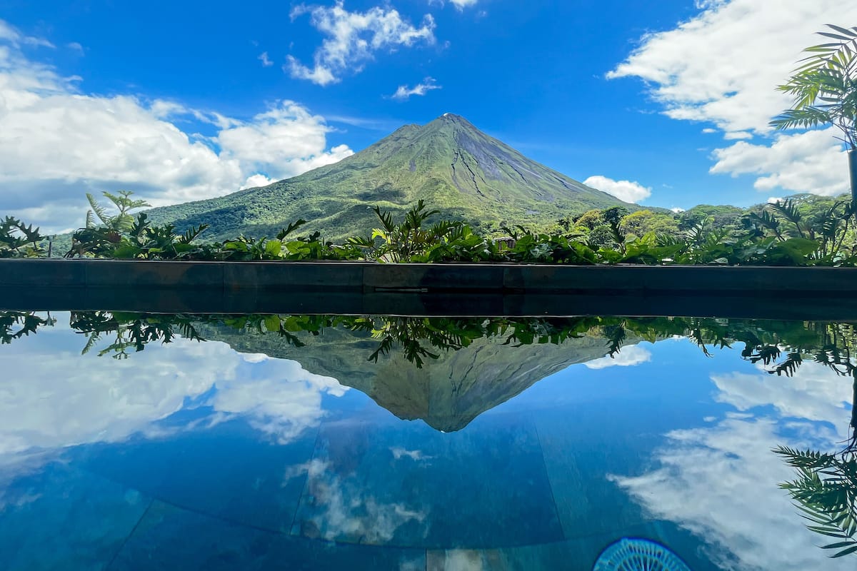 A mountain with a pool reflecting its image, surrounded by greenery.