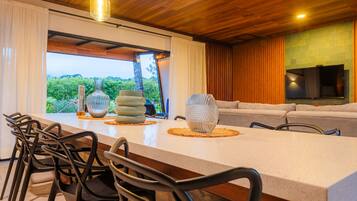 A modern kitchen with a large island, black chairs, and a view of greenery outside.
