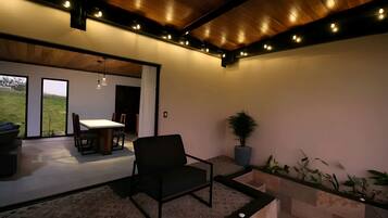 Ein modernes Interieur mit Holzbalkendecke, einem Essbereich mit Tisch und Stühlen sowie einer Sitzecke mit Sessel und Topfpflanzen.