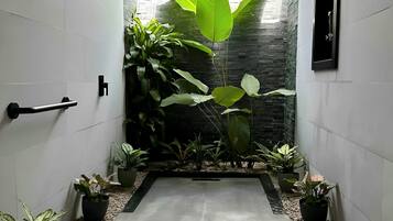 A modern hallway with a concrete floor, white walls, and a stone wall at the end. There are potted plants on either side and a black door handle on the left.