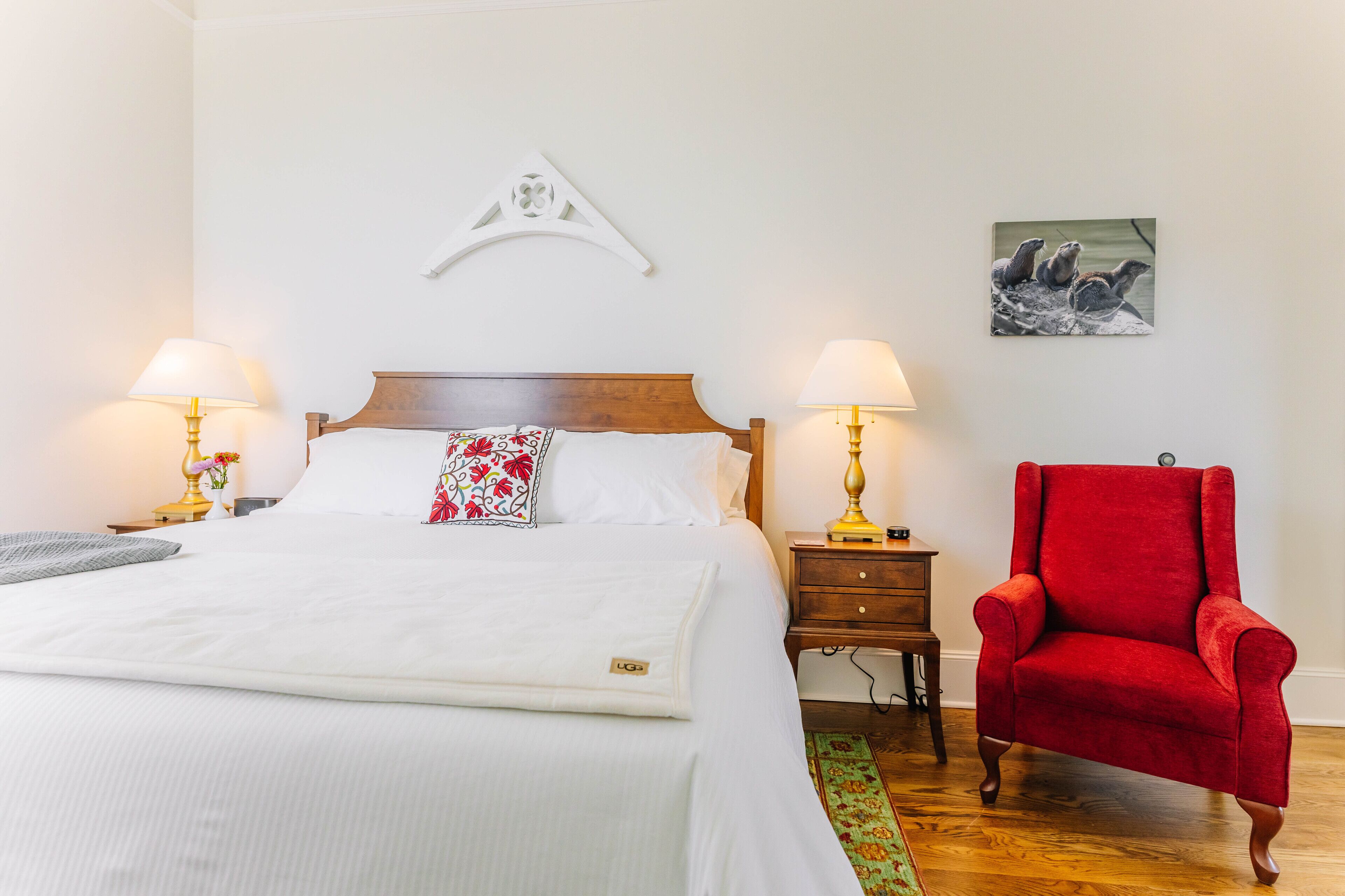 Un lit bien fait, avec du linge de lit blanc, un coussin à motifs floraux rouges et deux lampes de chevet.