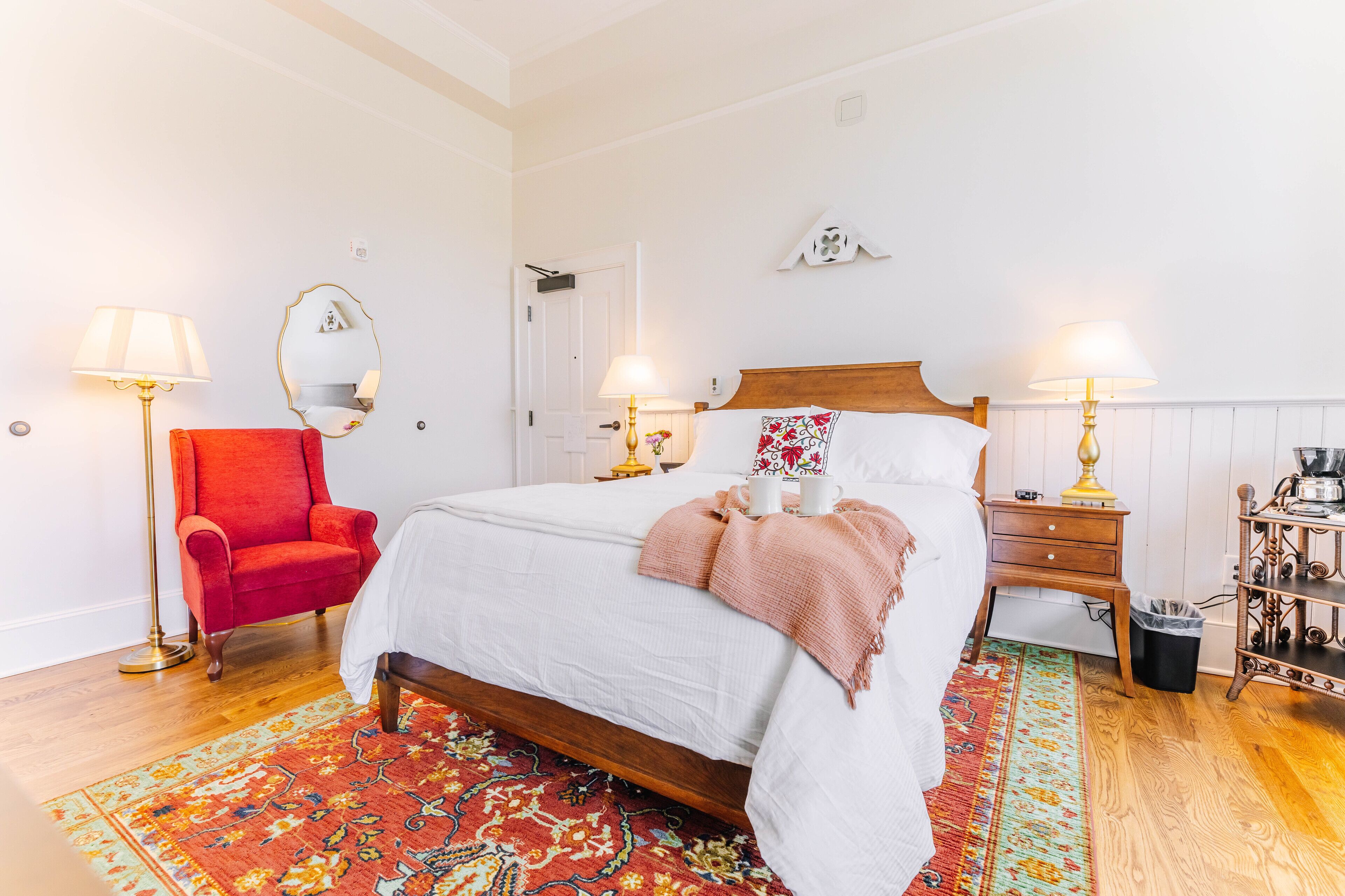 A neatly arranged bedroom with a single bed, a red armchair, two bedside tables with lamps, and a patterned rug.