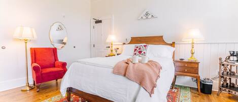 A neatly arranged bedroom with a single bed, a red armchair, two bedside tables with lamps, and a patterned rug.
