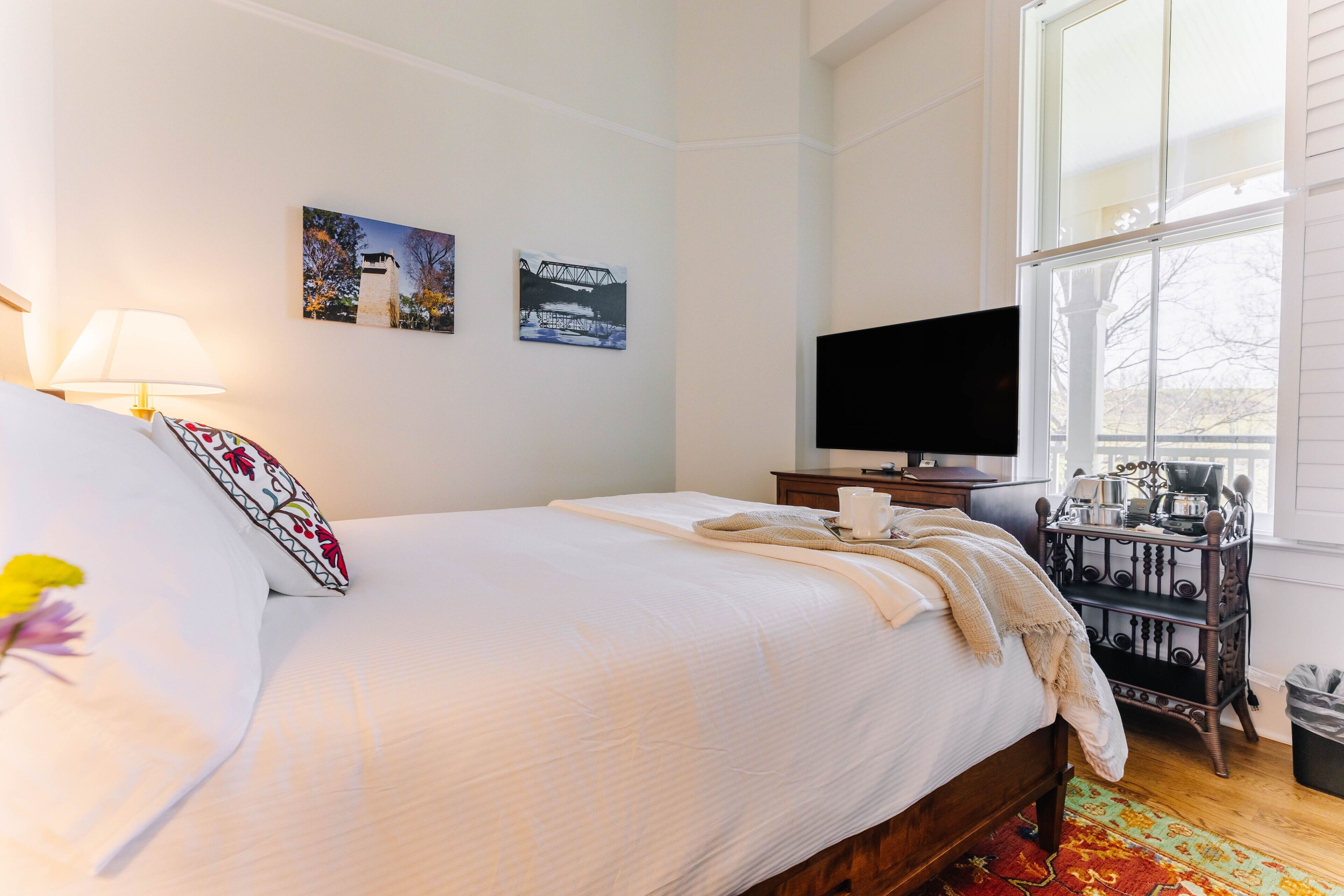 Una habitación de hotel con una cama, televisión, cafetera y obras de arte en la pared.