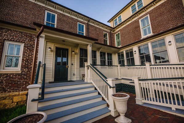 A two-story brick house with a front porch, white railings, and a black door.