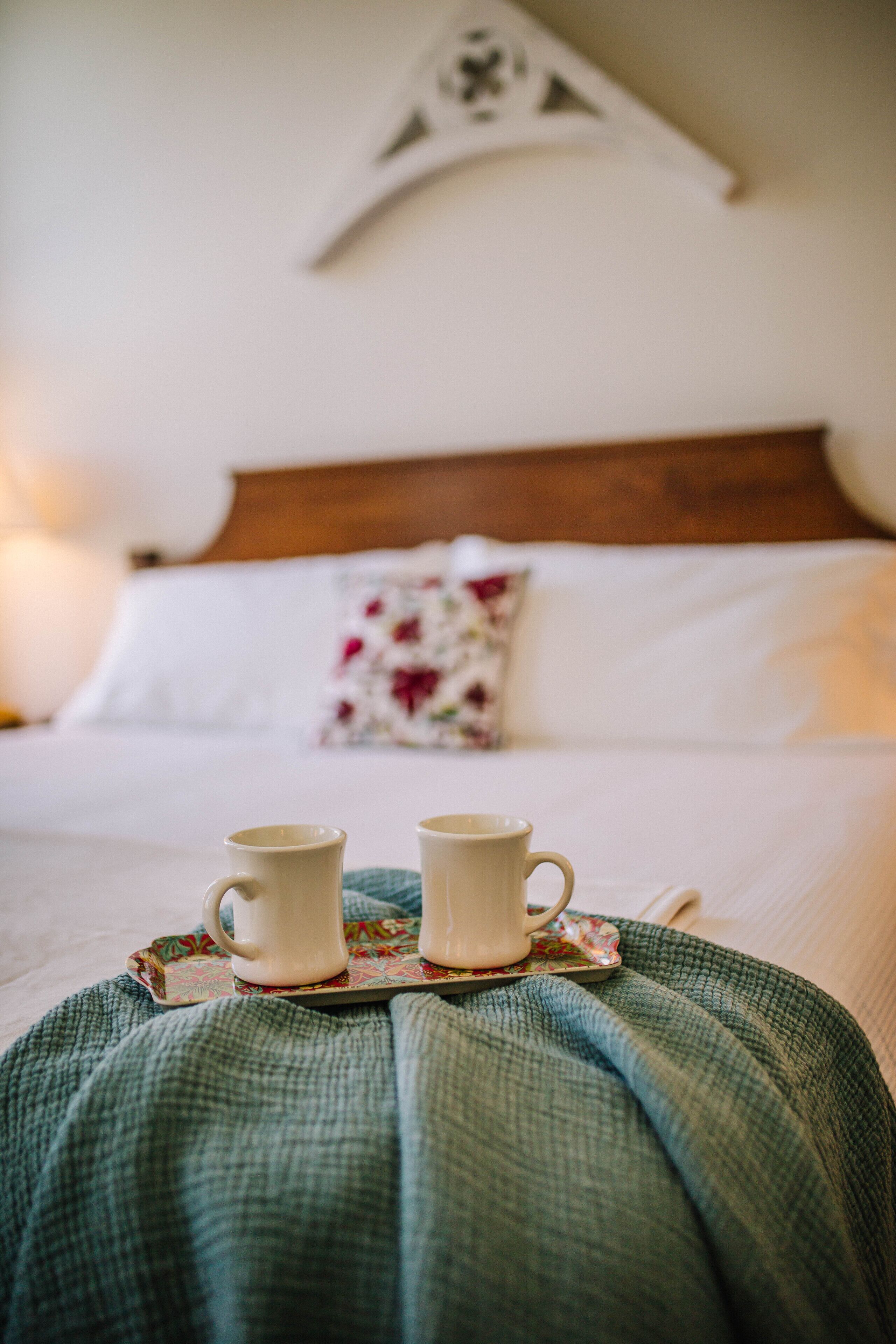 Una cama con dos tazas blancas sobre una bandeja, una manta verde y un cabecero de madera.