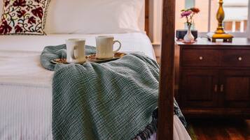 A neatly made bed with a green blanket, two white cups, and a tray.