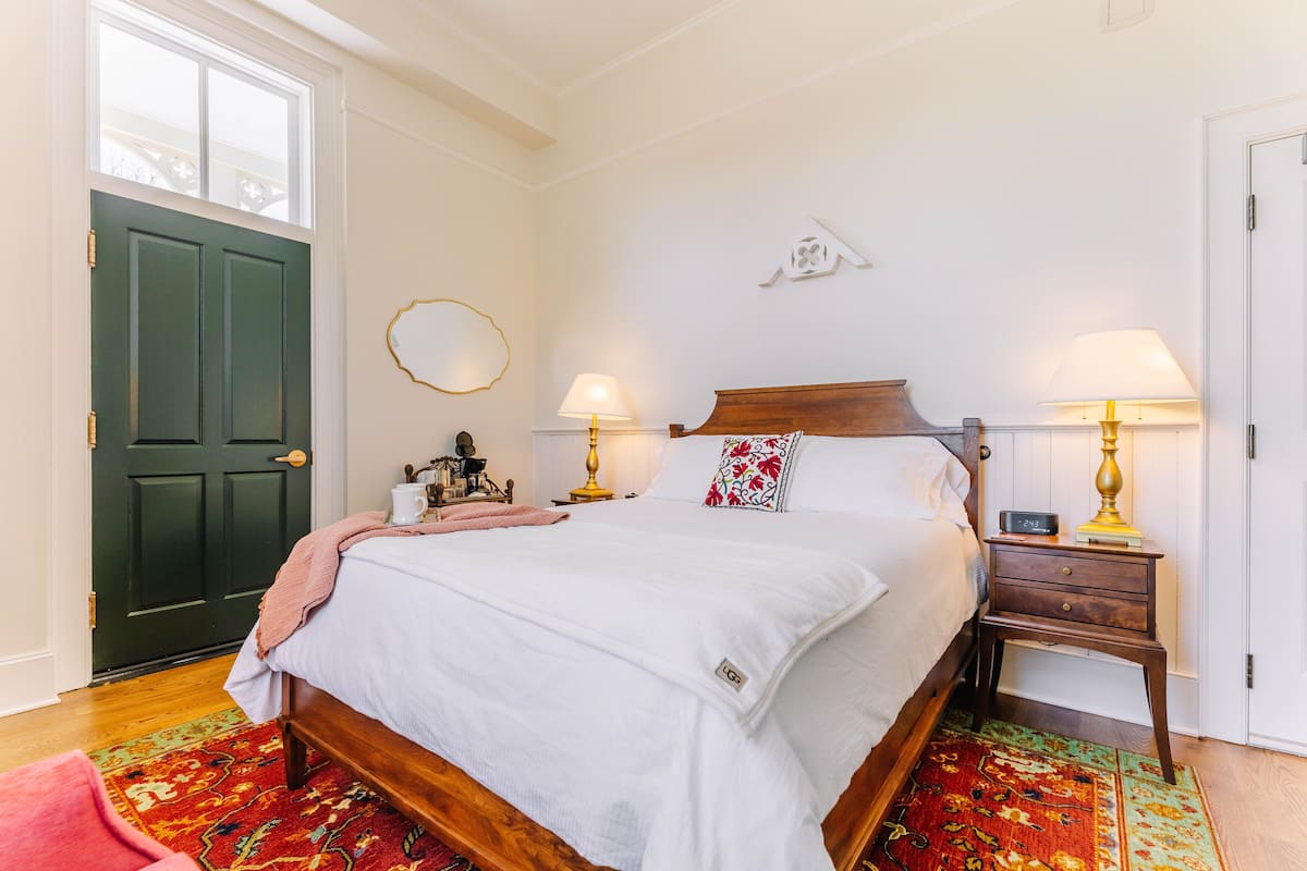 A neatly arranged bedroom with a bed, two bedside tables with lamps, a door, and a wall-mounted decoration.