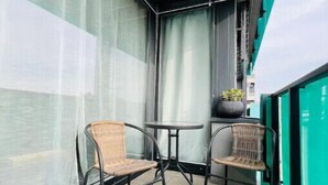 A balcony with two wicker chairs and a small table, a potted plant, and sheer curtains.