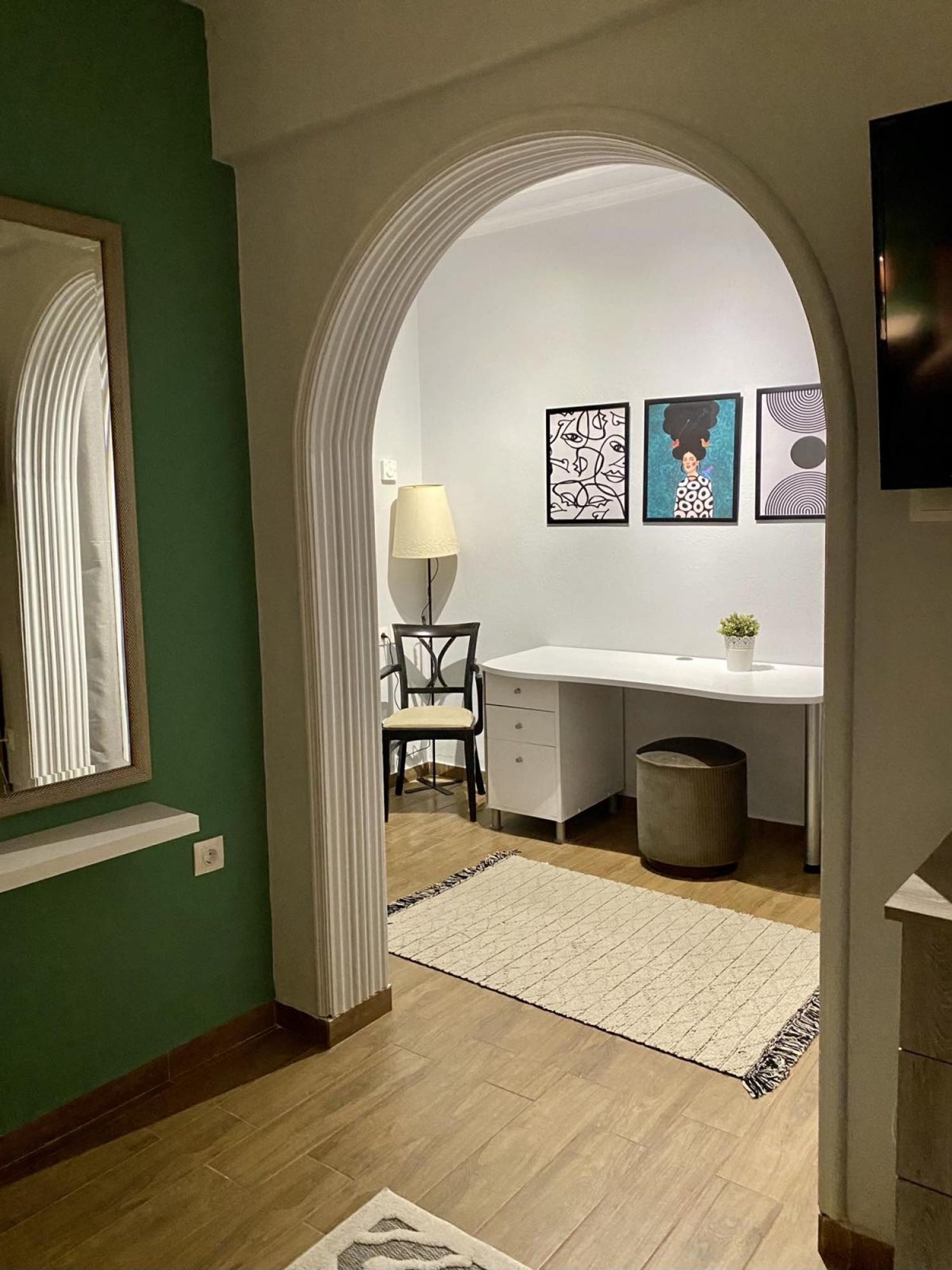 Un pasillo que conduce a una habitación con un escritorio, una silla, una lámpara y una obra de arte en la pared.