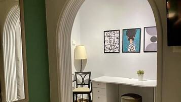 Un pasillo que conduce a una habitación con un escritorio, una silla, una lámpara y una obra de arte en la pared.