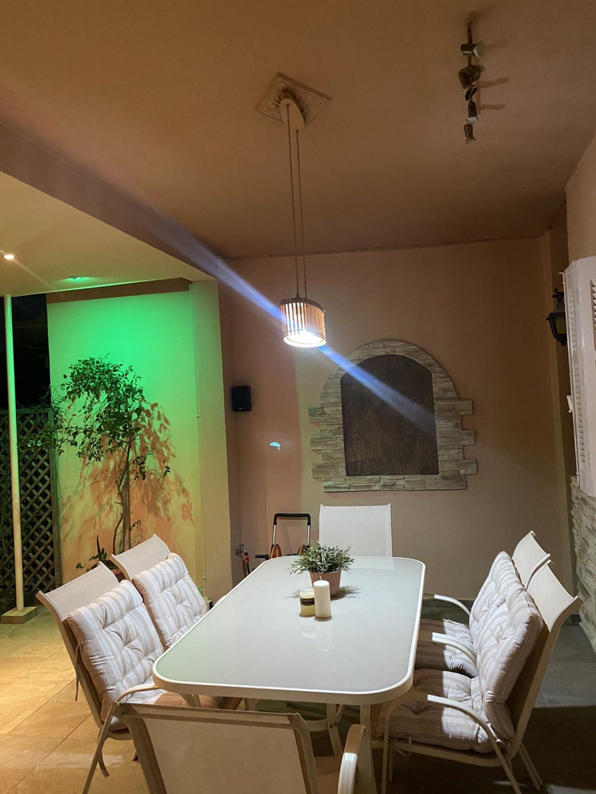 Un comedor con una mesa y sillas blancas, una lámpara colgante y una pared de piedra con una ventana.