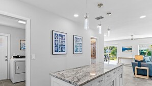 A modern kitchen with a marble countertop, white cabinetry, and pendant lighting. - Amazing Home on the Intracoastal Waterway! (Indian Rocks Beach)