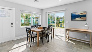 A modern dining area with a wooden table and chairs, large windows with a view of greenery, and a painting on the wall. - Amazing Home on the Intracoastal Waterway! (Indian Rocks Beach)