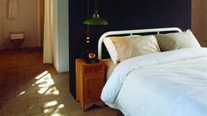 A bedroom with a bed, a nightstand with a lamp, a wooden floor, and a dark wall. - Maison Couturier, San Rafael, a Member of Design Hotels (San Rafael)