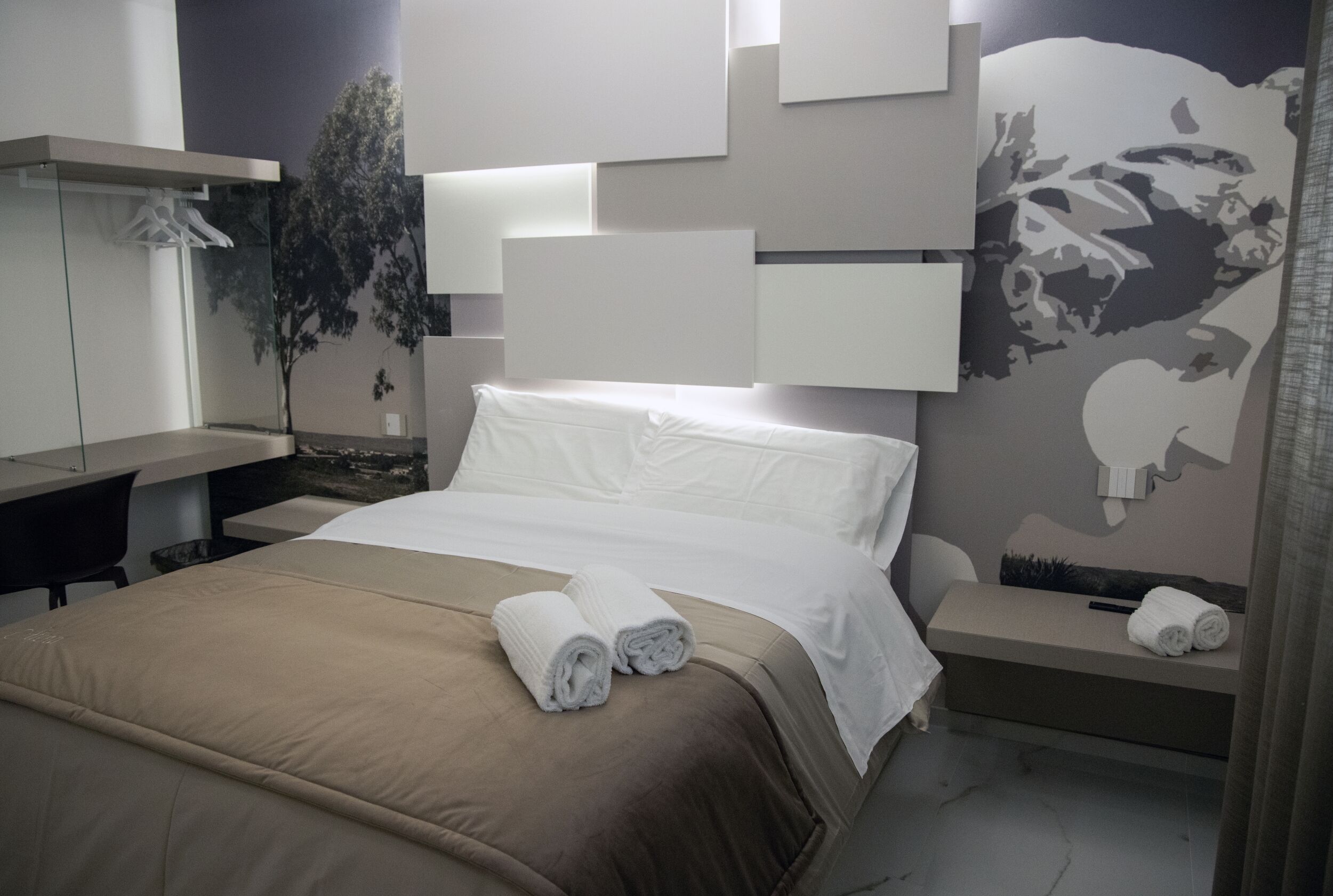 A modern hotel room with a neatly made bed, a desk, and a large wall mural.