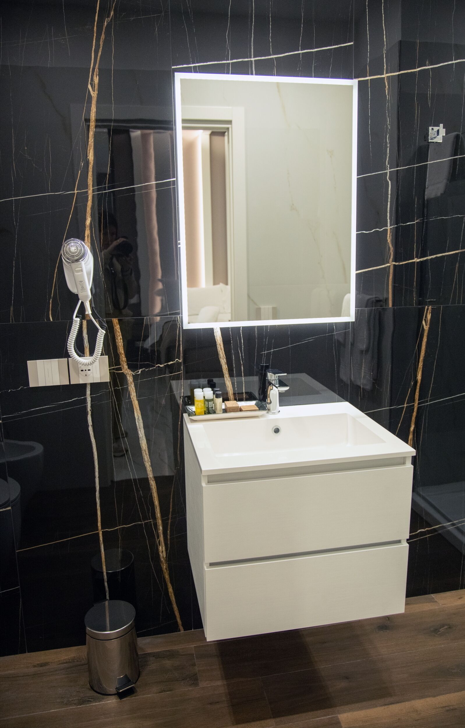 Ein Badezimmer mit einem weißen Waschtisch, einem Spiegel und einem Haartrockner auf einem Stativ.