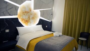 Ein modernes Hotelzimmer mit Bett, Nachttisch, Stuhl und einem großen Fenster mit Vorhängen.