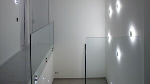 A modern interior with a glass railing, a door, and recessed lighting on the walls. - Lauria Luxury Room (Gela)