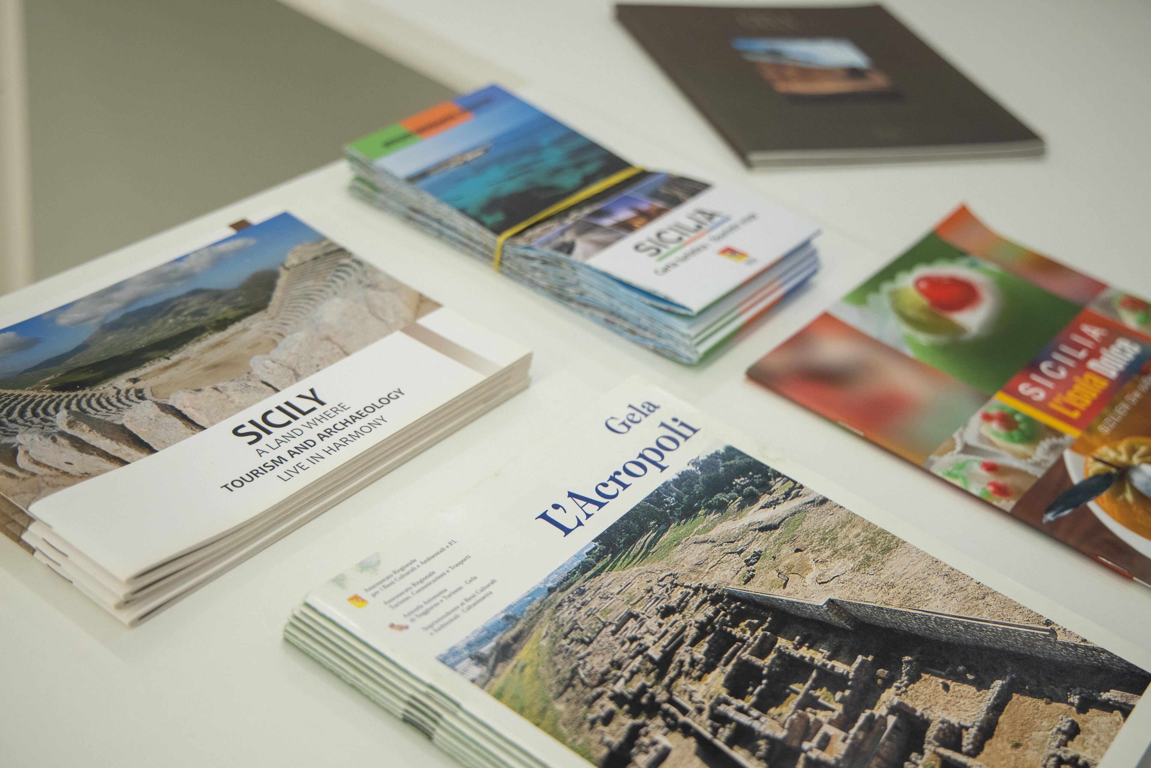 A table with several brochures and magazines, including one titled "Sicily" and another titled "Acropoli".