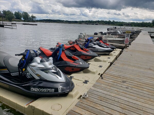 Varias motos acuáticas alineadas en un muelle de madera junto al agua.