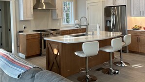 A modern kitchen with a central island, stainless steel appliances, and pendant lighting. - New Maine Private Lake House (Waltham)