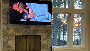 A stone fireplace with a TV mounted above it displaying a scene with a document labeled "FINAL NOTICE". - New Maine Private Lake House (Waltham)