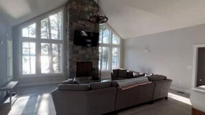 A spacious living room with a large window, a stone fireplace, and a modern sofa. - New Maine Private Lake House (Waltham)