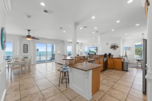 Uma cozinha espaçosa com uma ilha grande, uma área de refeições com vista e uma sala de estar com televisão.