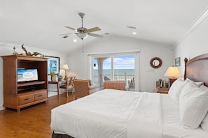 Quarto com uma cama, televisão, ventoinha no teto, escrivaninha com cadeira e vista para o oceano.