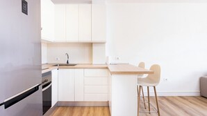 Eine moderne Küche mit weißen Schränken, einem Edelstahl-Kühlschrank, einer Holz Arbeitsplatte und einem Barhocker.