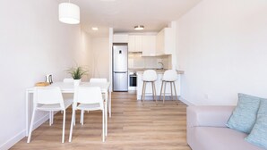 Eine moderne Küche mit weißen Schränken, einem Edelstahlkühlschrank und einem Essbereich mit weißen Stühlen und einem Tisch.