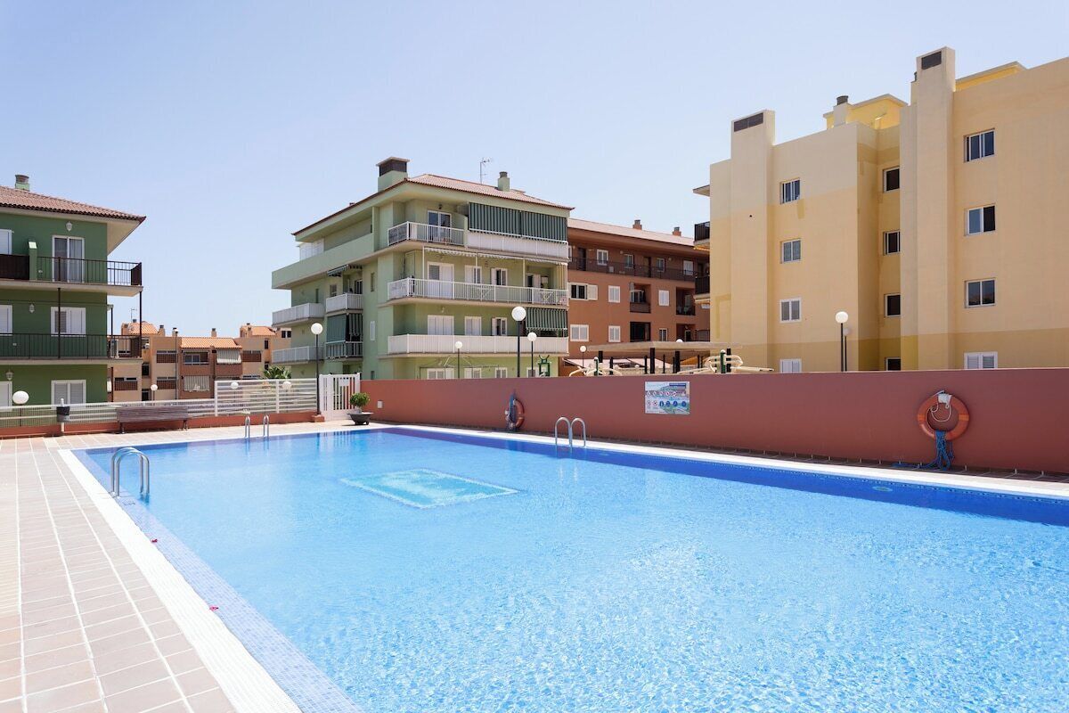 A swimming pool with a tiled deck, surrounded by multi-story buildings with balconies and windows.