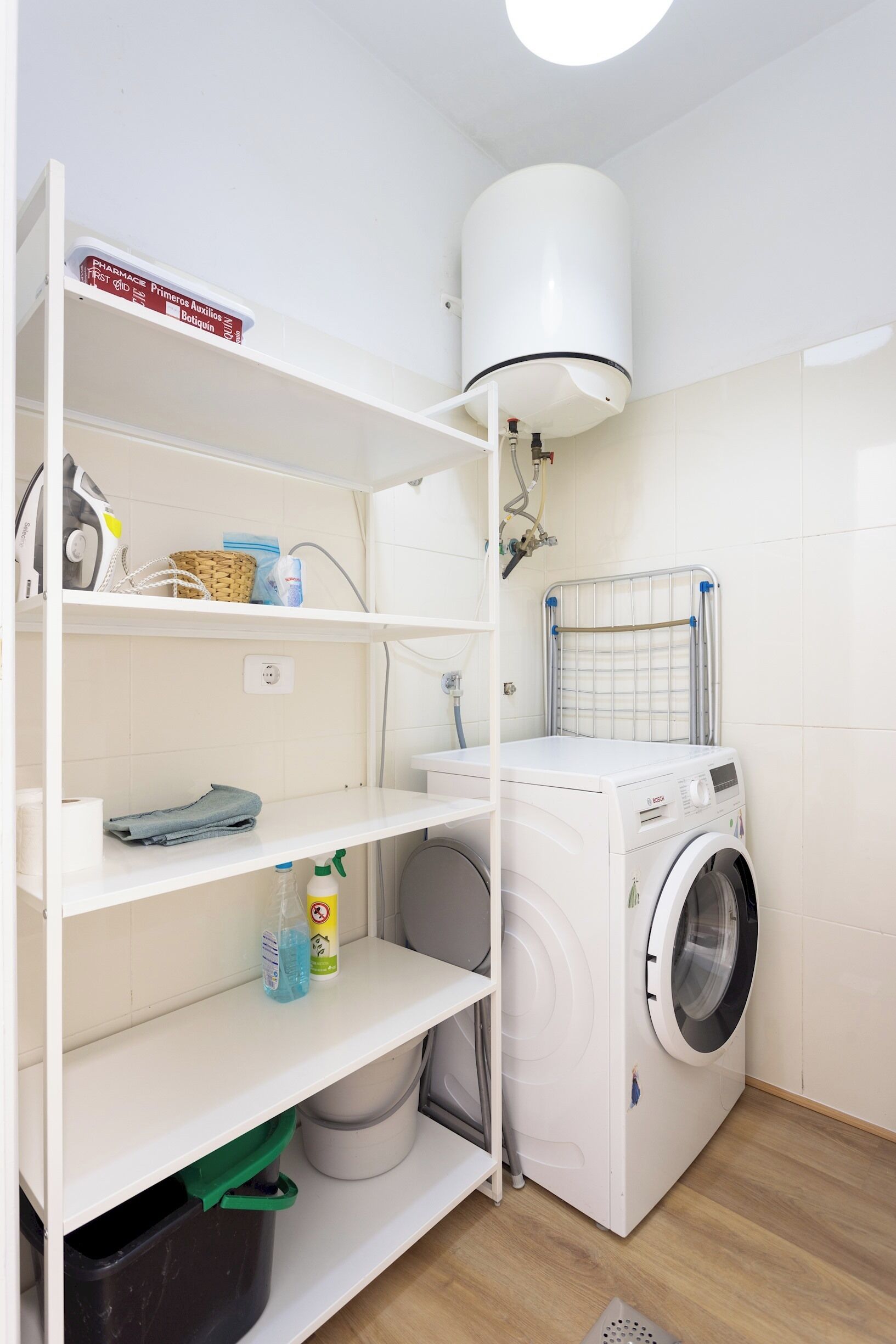 A laundry room with a washing machine, shelves with laundry supplies, a basket, and a water heater.