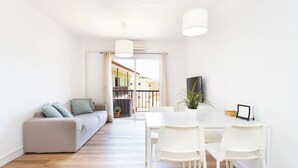 Ein modernes Wohnzimmer mit einer Couch, einem Esstisch und Stühlen. Durch die Tür ist ein Balkon zu sehen.
