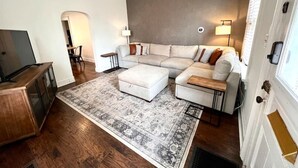 A modern living room with a sectional sofa, ottoman, and a patterned rug. - 886 Macon (2 bdrm) · Walkable German Village home w/ fenced yard (Columbus)